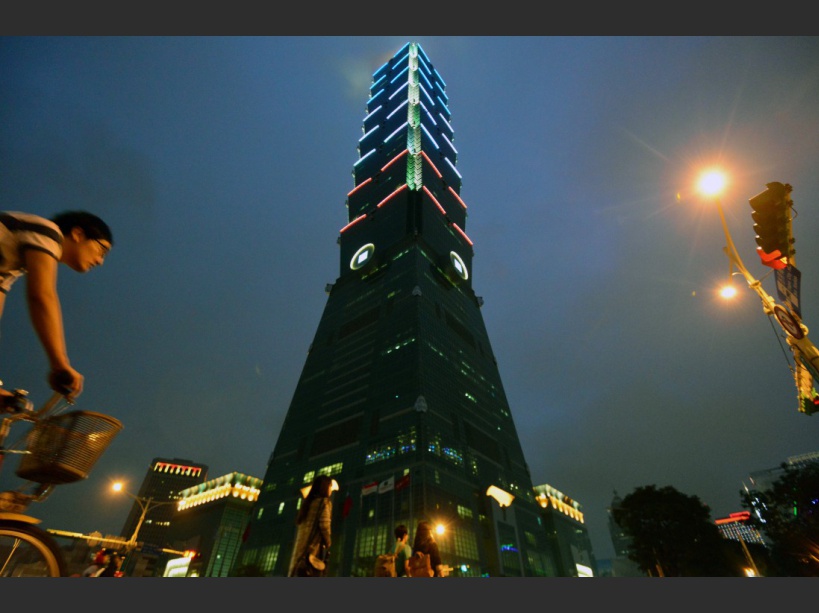 A man rides next to the Taipei 101 building in Taipei on November 14, 2015, as it lit up with the colours of the French flag in honour of the victims killed in a spate of coordinated attacks that left 128 dead and 180 injured in Paris late on November 13. French President Francois Hollande on November 14 declared three days of national mourning following the deadly Paris attacks. AFP PHOTO / Sam Yeh