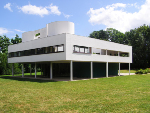 Image de la villa Savoye, cube blanc posé sur pilotis sur une grande pelouse arborée.